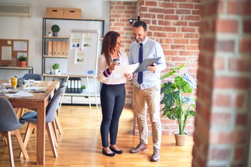 Two middle age business workers smiling happy and confident. Standing with smile on face working together holding clipboard and drinking coffee at the office