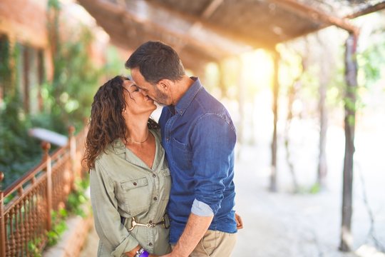 Middle age beautiful couple smiling happy and confident at town park. Standing with smile on face hugging and kissing