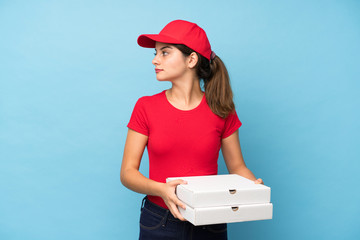 Young woman holding a pizza over isolated pink wall looking side