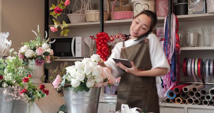 Woman taking order from customer at her flower shop. She using smartphone to talking with customer with confident.