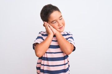 Beautiful kid boy wearing casual striped t-shirt standing over isolated white background sleeping tired dreaming and posing with hands together while smiling with closed eyes.