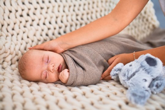 Young beautifull woman and her baby on the sofa over blanket at home. Newborn and mother relaxing and resting comfortable