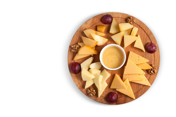 Fototapeta premium Cheese platter on a round wooden plate with walnuts, honey and grapes. Isolated, horizontal orientation, top view, copy space
