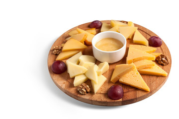 Cheese platter on a round wooden plate with walnuts, honey and grapes. Isolated, horizontal orientation, copy space