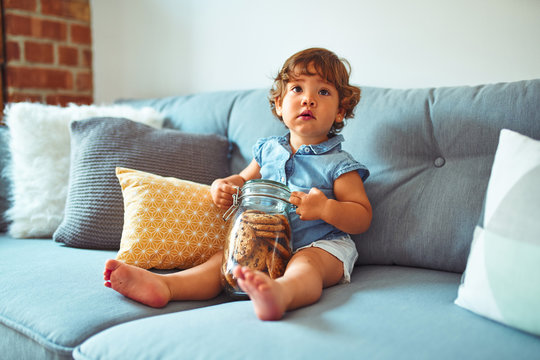 Beautiful toddler child girl holding jar of cookies sitting on the sofa