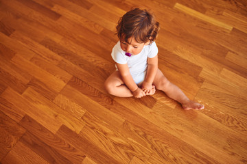 Beautiful toddler child girl wearing white t-shirt sitting on the floor using pacifier