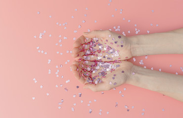 abstract image with hands strewn with small shiny hearts on a pink background.