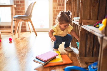 Beautiful toddler taking books of shelving at kindergarten