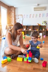 Young beautiful teacher and toddler playing with building blocks toy at kindergarten