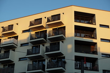 Modernes Wohnhaus in Beige und Naturfarben mit Balkons vor blauem Himmel im Licht der Abendsonne in...
