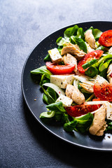 Caesar salad -  barbecue chicken breast, vegetables and feta cheese on black stone background