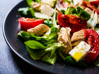 Caesar salad -  barbecue chicken breast, vegetables and feta cheese on black stone background