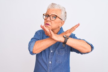 Senior grey-haired woman wearing denim shirt and glasses over isolated white background Rejection expression crossing arms doing negative sign, angry face