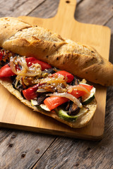 Vegan sub sandwich with grilled vegetables on wooden background
