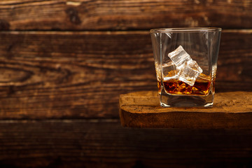 Whiskey with ice or brandy in a glass and a square carafe on an old wooden background. Whiskey with ice in a glass. Whiskey or cognac. Selective focus.