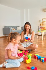 Obraz na płótnie Canvas Beautiful teacher and blond toddler girl building tower using plastic blocks at kindergarten