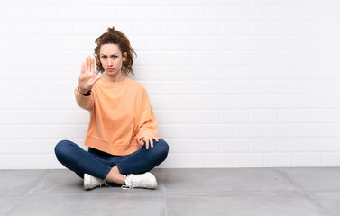 Young woman with curly hair sitting on the floor making stop gesture with her hand