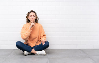 Young woman with curly hair sitting on the floor doing silence gesture