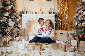 A loving couple enjoys each other on New Year's Eve in a cozy home environment. New Year's love story. Beautiful couple in sweaters with hearts posing in a studio. A guy with a girl is celebrating