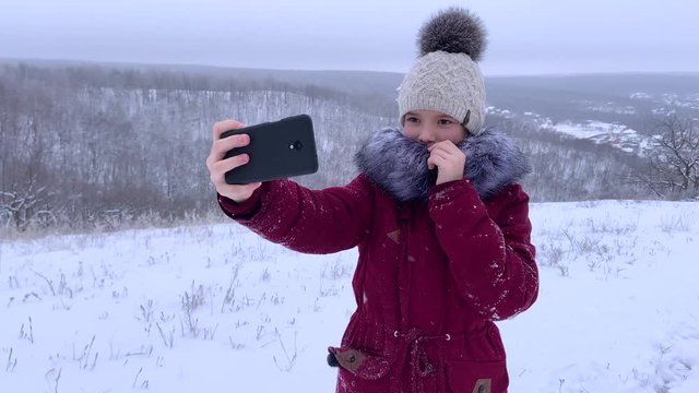 teenager young caucasian girl taking selfie photos on smartphone and posing for a photo in the Russian winter snowy forest. Healthy open air spending holidays or weekend outdoors in cold weather.