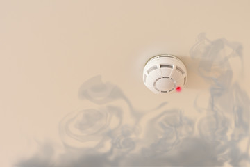 Smoke detector on the white ceiling for prevention fire with red emergency lamp and dark fume. Fire alarm for home, offices and hotels.