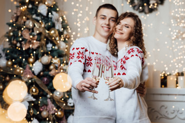 Couple knocking on champagne glasses. The guy kisses his girlfriend in the forehead.  New Year's love story. Photo session in the studio. Merry Christmas.  Valentines day. Weekend. Romantic date. 