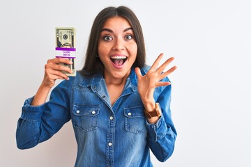 Obraz premium Young beautiful woman holding dollars standing over isolated white background very happy and excited, winner expression celebrating victory screaming with big smile and raised hands