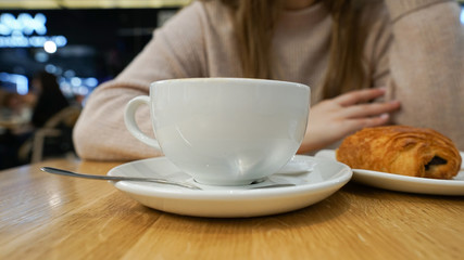 Cup of hot coffee on table in cafe with young woman. Coffee break. morning coffee and croissant with chocolate