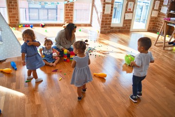 Fototapeta na wymiar Beautiful teacher and group of toddlers playing around lots of toys at kindergarten