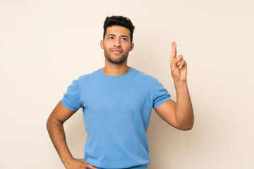 Young handsome man over isolated background with fingers crossing and wishing the best