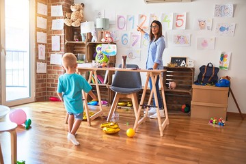 Young caucasian child playing at playschool with teacher. Mother and son at playroom around toys showing numbers on the wall