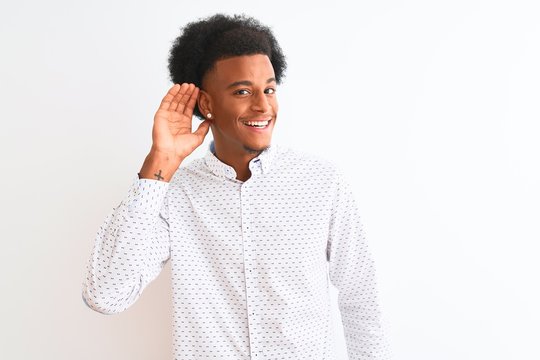 Young african american man wearing elegant shirt standing over isolated white background smiling with hand over ear listening an hearing to rumor or gossip. Deafness concept.