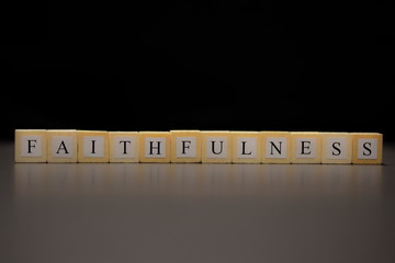 The word FAITHFULNESS written on wooden cubes isolated on a black background..