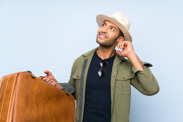 Young handsome man holding a vintage briefcase over isolated blue background having doubts and with...