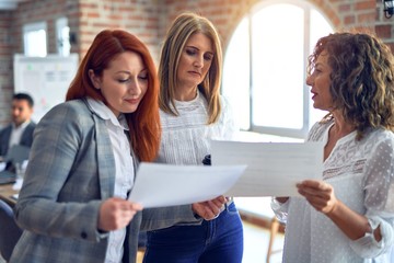 Beautiful businesswomen smiling happy. Standing with smile on face working together reading documents at the office