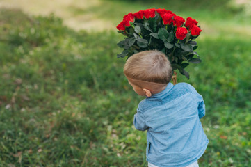 Boy with a bouquet of red roses in hands on a background of greenery.