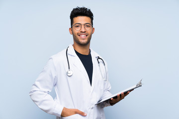 Young doctor man over isolated blue wall
