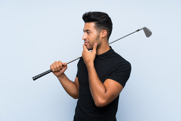 Handsome young man playing golf over isolated blue background looking side