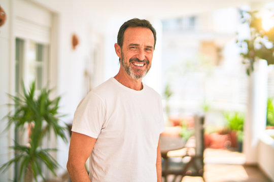 Middle age handsome man wearing casual t-shirt standing on terrace smiling
