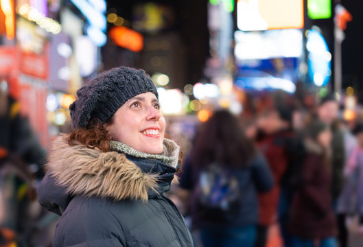 Amazed woman with warm clothes looking at the lights and the crowd in Times Square while sightseeing new york during winter season. Selective focus.