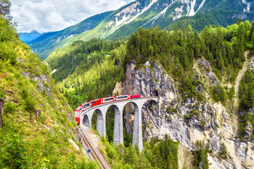 Landwasserviadukt im Sommer, Filisur, Schweiz. Es ist Wahrzeichen der Schweizer Alpen. Schöne Alpenlandschaft. Roter Zug des Bernina Express auf Eisenbahnbrücke in den Bergen.