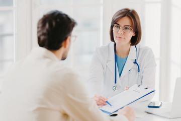 Fototapeta premium Female general practitioner explains which prescribed medicine patient should buy, gives medical visit consultation. Male clinic visitor tells about health complaints to therapist. Healthcare concept
