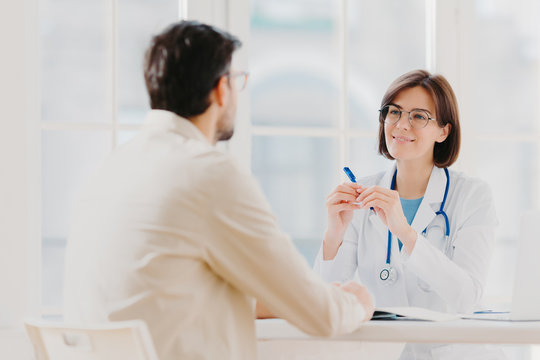 Heath Care And Medical Consultancy Concept. Skilled Therapist In White Uniform Talks With Patient, Writes Down In Medical History, Listens Attentively All Symptoms, Tries To Prevent Serious Disease