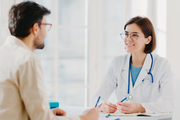 Photo of male patient writes all details makes notes during consultancy with doctor sit in spacious...