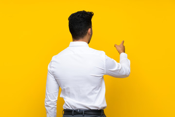 Young handsome man over isolated yellow background pointing back with the index finger