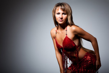 Young slim beautiful woman with long hair in sexy red shiny costume standing in dancing pose over dark background