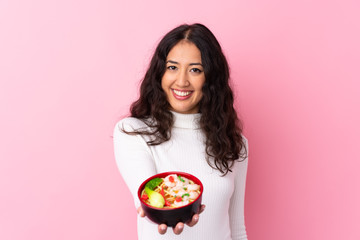 Mixed race woman holding a bowl full of noodles over isolated pink background with happy expression