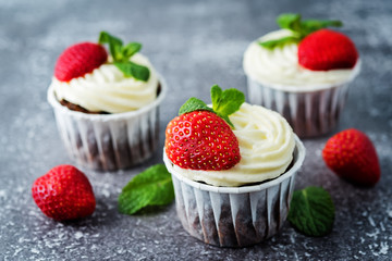 Chocolate cupcakes with cream cheese frosting, mint leaves and strawberries