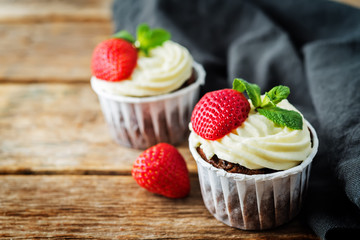 Chocolate cupcakes with cream cheese frosting, mint leaves and strawberries