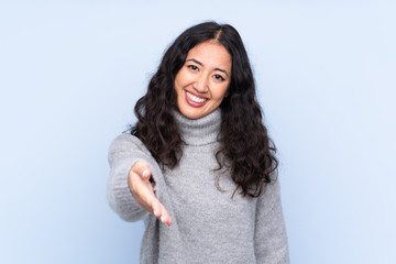 Spanish Chinese woman over isolated blue background shaking hands for closing a good deal